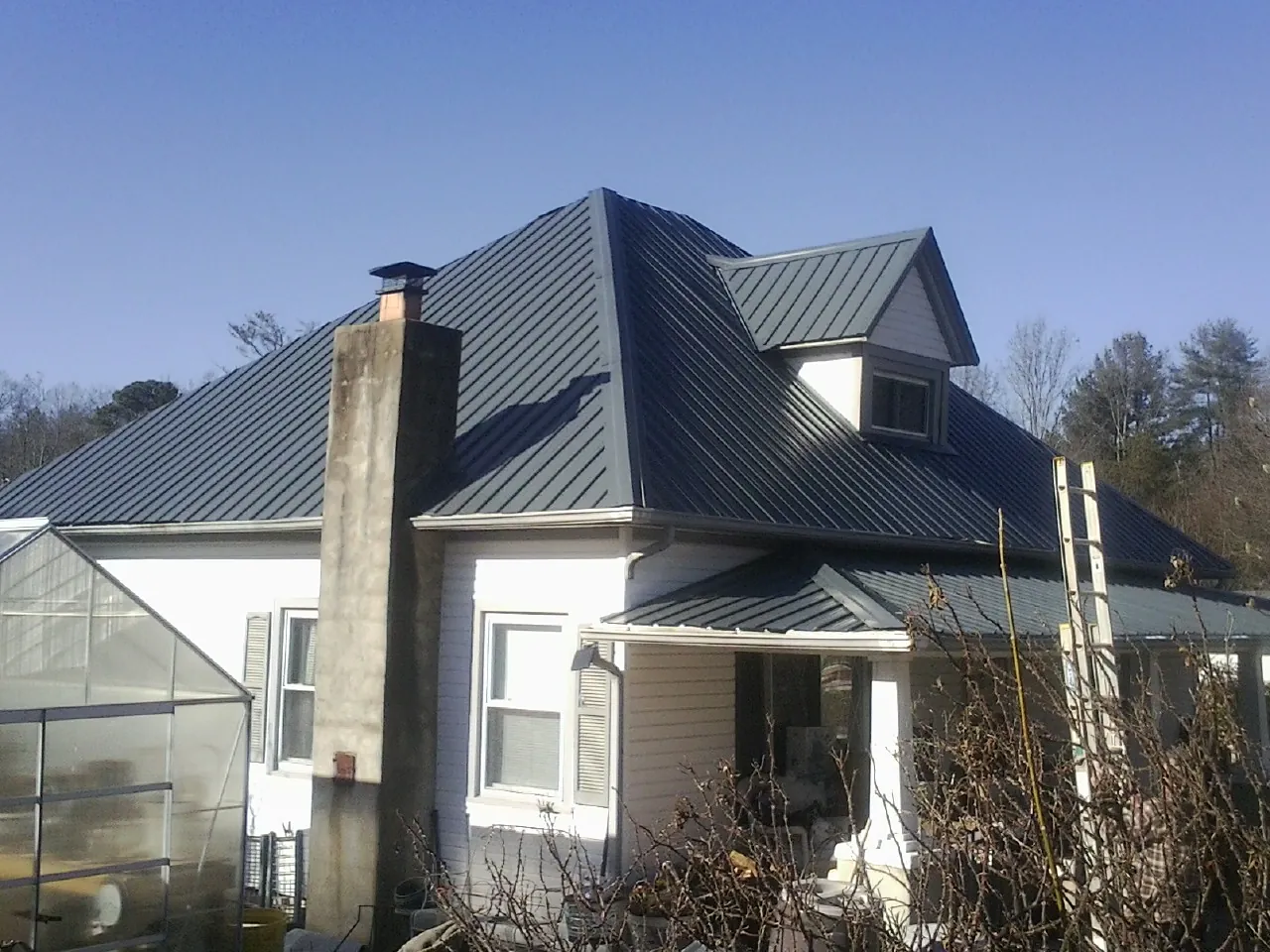 Dark blue standing seam metal roof on a white farmhouse with dormer — Slate & Tile Roof Repair by Roofing Brothers in Silver Point
